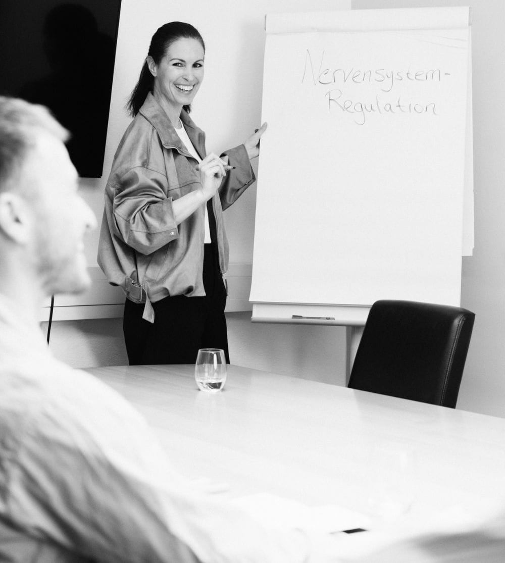 Trainerin für Nervensystem-Regulation leitet einen Workshop für Unternehmen und Teams vor einem Flipchart.